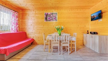 A wooden interior with a red sofa, a dining table with chairs, a cabinet, and a painting on the wall.