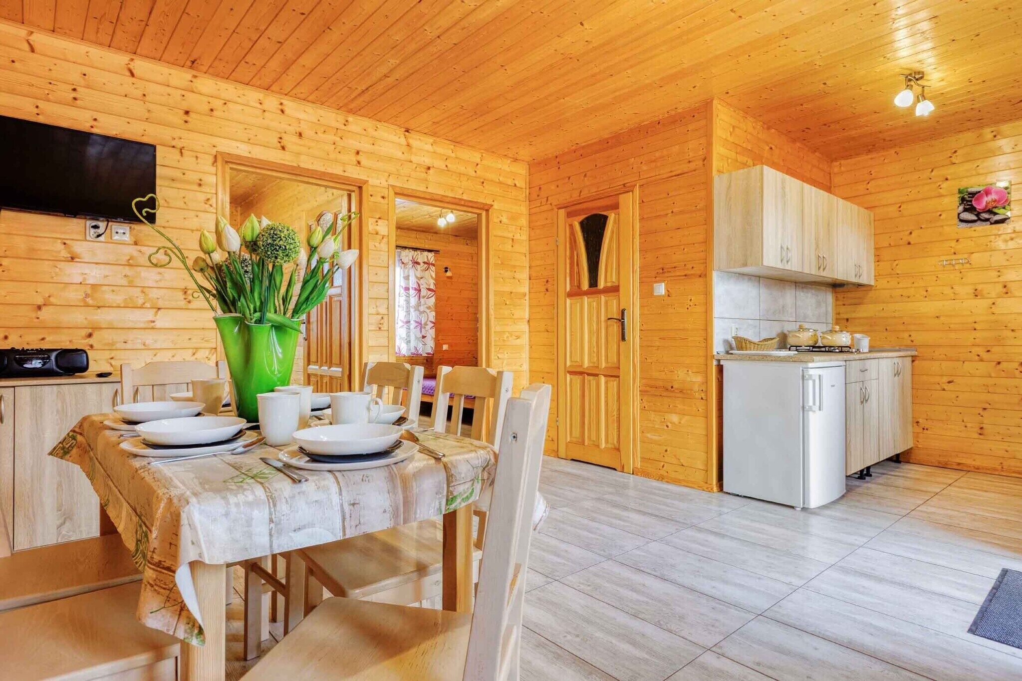 A wooden cabin with a dining area, kitchen, and a TV mounted on the wall.