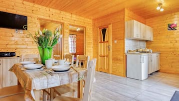 A wooden cabin with a dining area, kitchen, and a TV mounted on the wall.