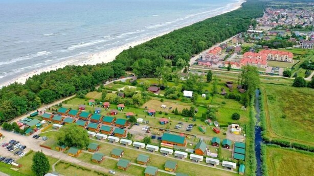 An aerial view of a coastal area with a beach, a row of mobile homes, and a residential area with houses. - Elegant House with Terrace Near Sea (Karwia)