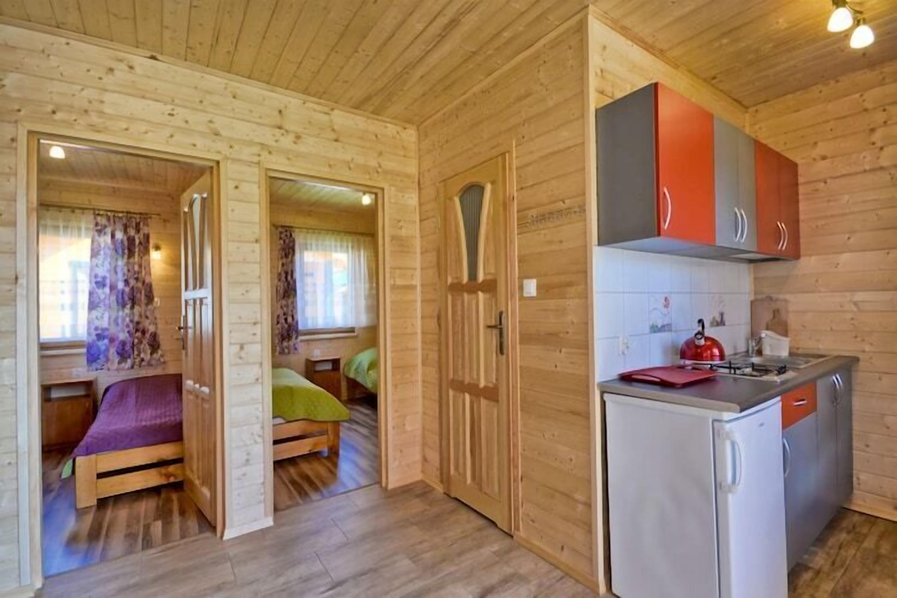 A compact wooden cabin with a small kitchenette, a single bed, and a bathroom.