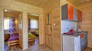 A compact wooden cabin with a small kitchenette, a single bed, and a bathroom.