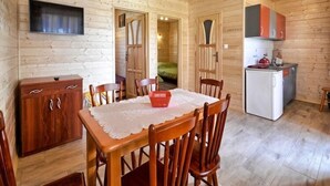 A wooden cabin interior with a dining table, chairs, a kitchen area with cabinets, a refrigerator, and a television mounted on the wall. - Elegant House with Terrace Near Sea (Karwia)