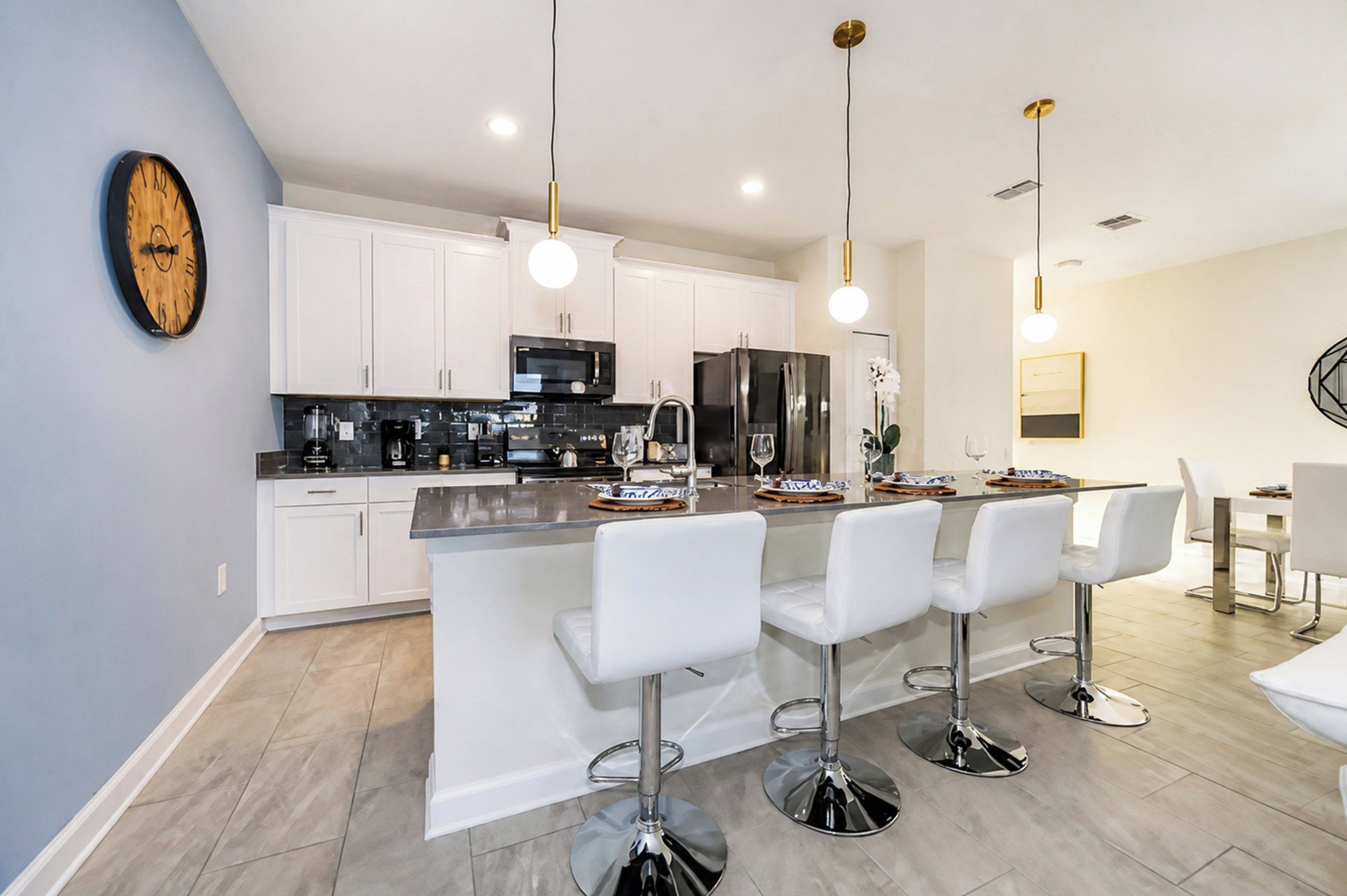 A modern kitchen with white cabinetry, a central island with bar stools, stainless steel appliances, and pendant lighting.
