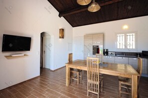 A modern kitchen with a wooden dining table and chairs, a built-in oven, and a TV mounted on the wall. - Peaceful stay: quiet villa, ideal for families or couples. 3 BEDS (Figari)