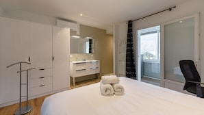 A modern hotel room with a large bed, a vanity with a mirror, a black chair, and a view of the outdoors through a sliding door. - La Source du Lac - Plage privée (Doussard)