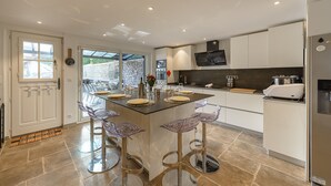 A modern kitchen with a central island, bar stools, and a dining area with a view of the garden. - La Source du Lac - Plage privée (Doussard)