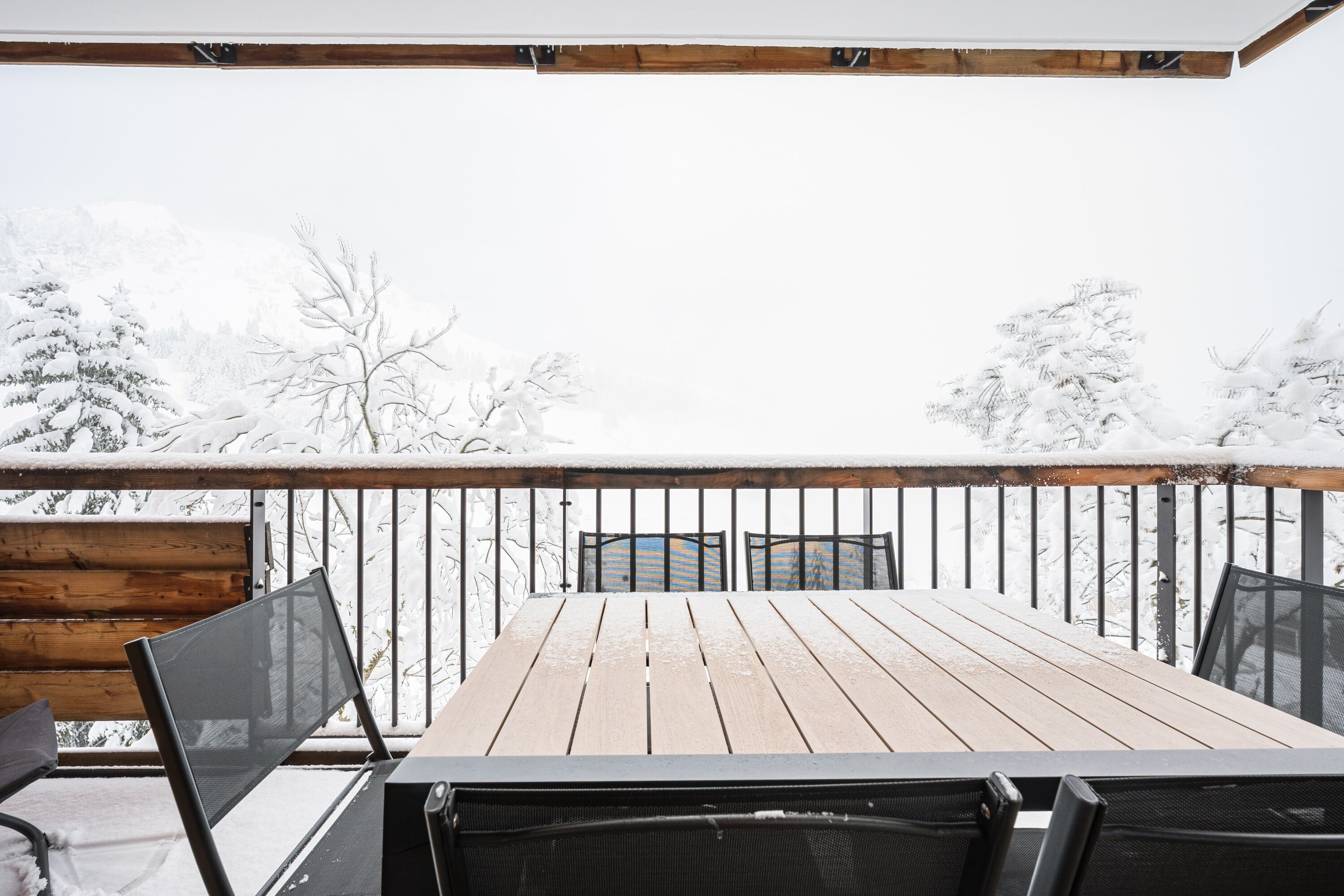 Una terraza de madera con una mesa y sillas, rodeada de árboles cubiertos de nieve.