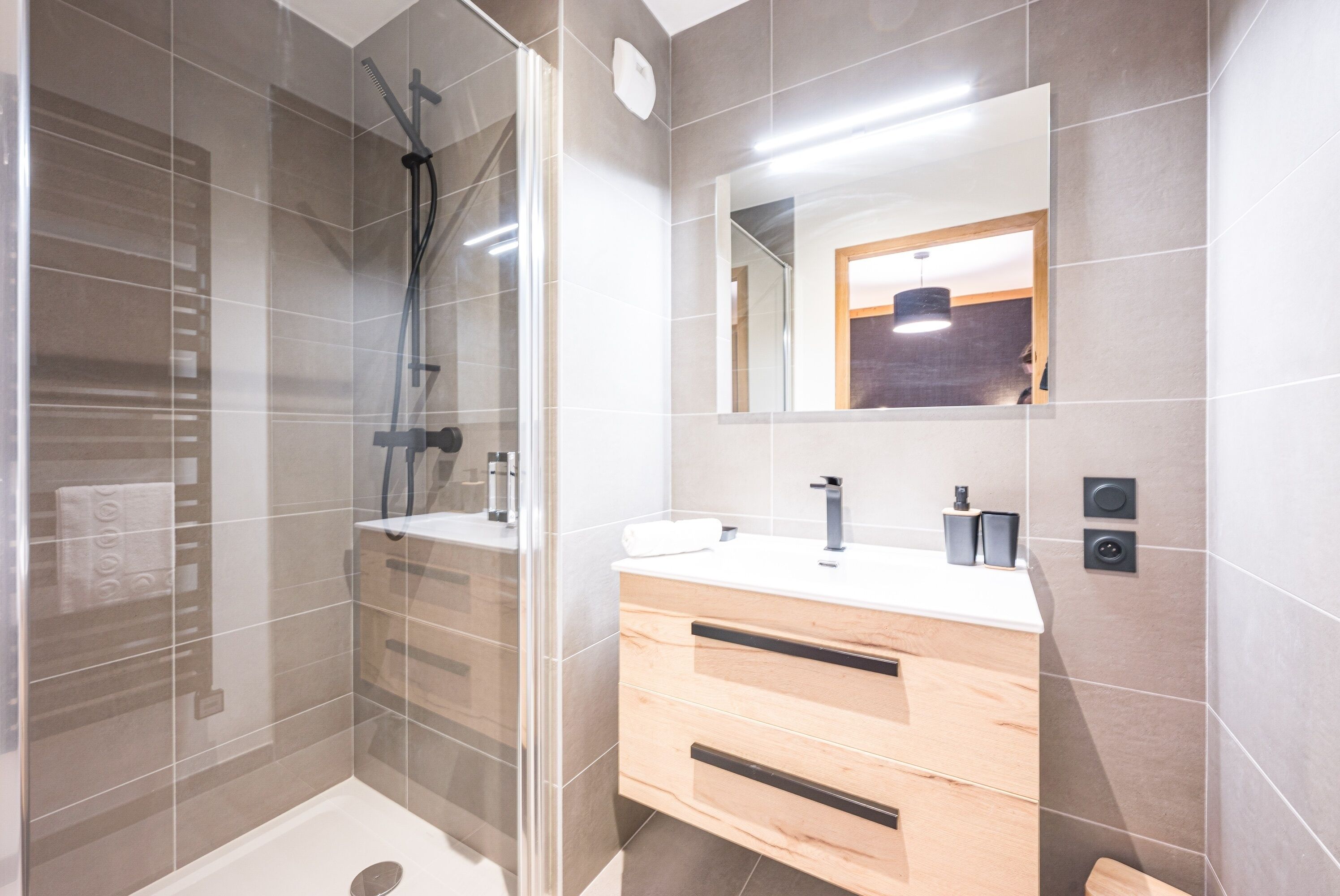 A modern bathroom with a glass shower enclosure, a wooden vanity with a sink, and a mirror above the vanity.