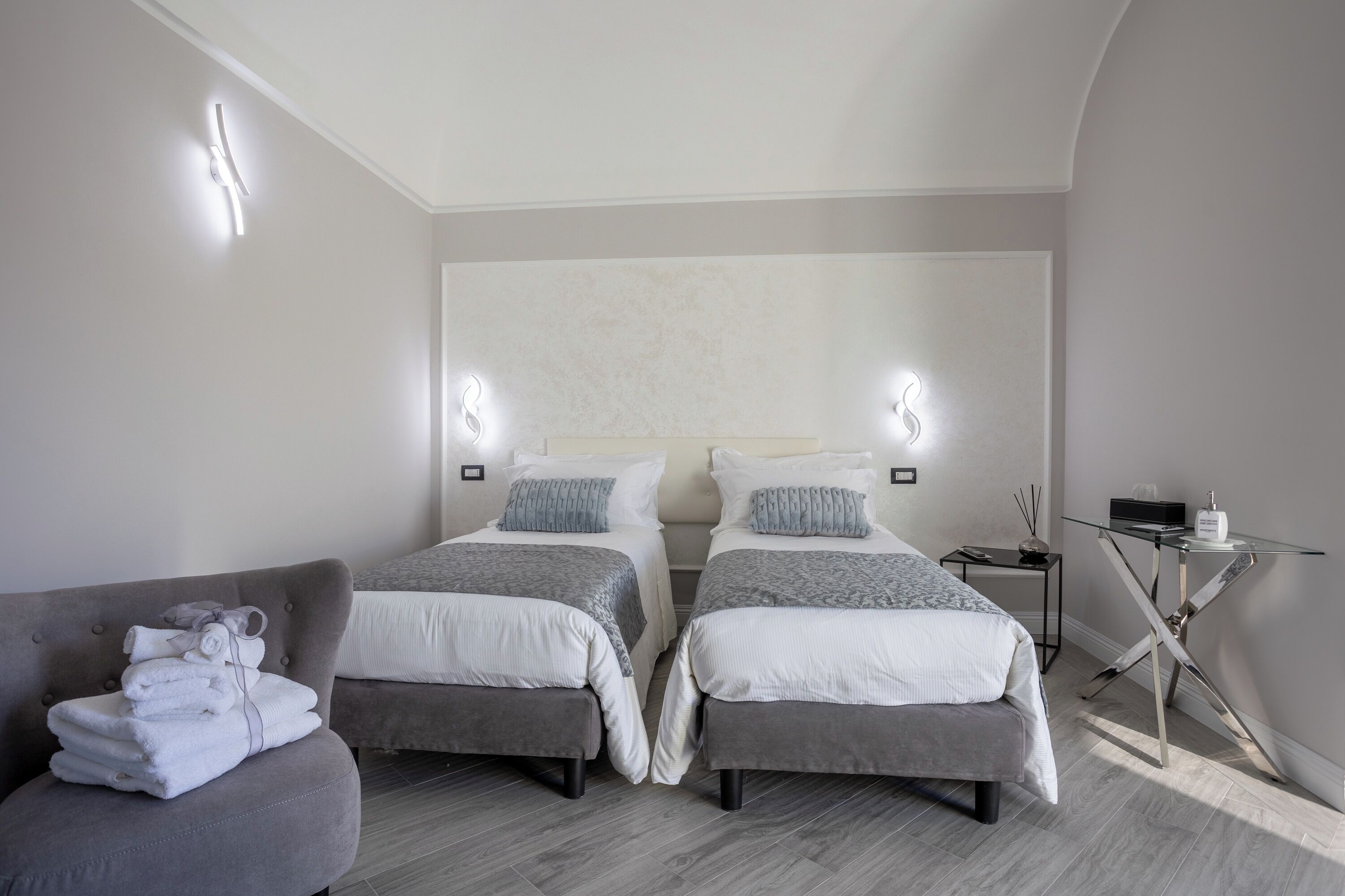 A modern hotel room with two beds, a seating area, and a small table with a lamp.