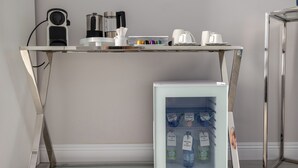 A modern kitchen with a glass-top table, a coffee machine, a kettle, and a mini-fridge with bottles. - Cozy studio apartment within walking distance of hospital (Vercelli)