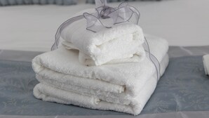 A stack of white towels with a transparent bow on a bed with a patterned bedspread. - Cozy studio apartment within walking distance of hospital (Vercelli)