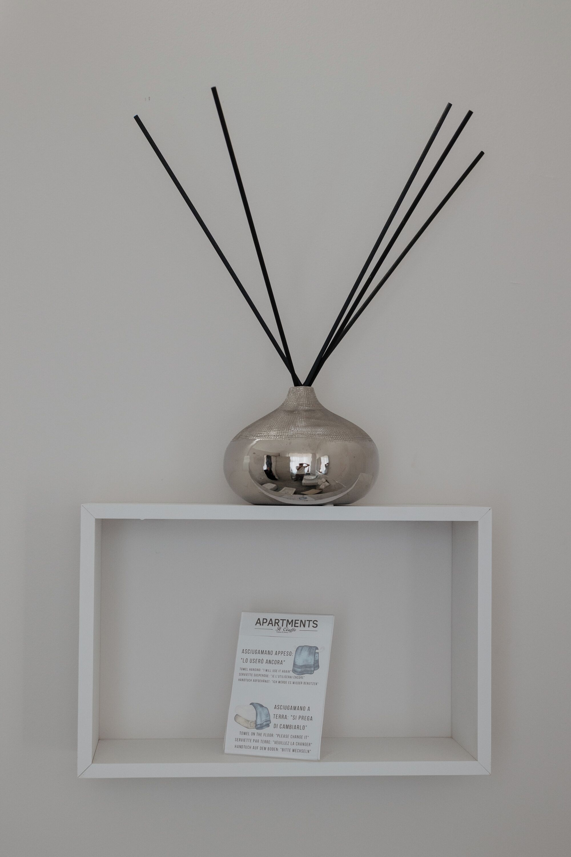 Ein weißes Regal mit einer silbernen Vase, die schwarze Äste enthält, und einer Karte mit Text und Illustrationen.