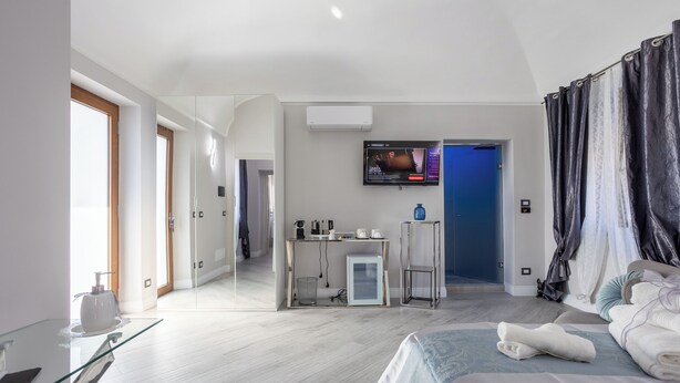A modern hotel room with a bed, a glass table, a desk with a computer, a TV on the wall, and a shower area. - Cozy studio apartment within walking distance of hospital (Vercelli)
