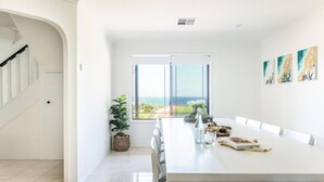Un vaste espace dédié à la salle à manger, avec une longue table, une plante en pot et une vue sur l’océan.