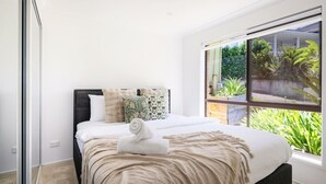 Une chambre moderne avec une grande fenêtre, un lit soigneusement fait et une vue sur la verdure environnante.