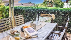 Un espace extérieur abrité, aménagé pour les repas, avec une table pour deux personnes, offrant une vue sur la côte.