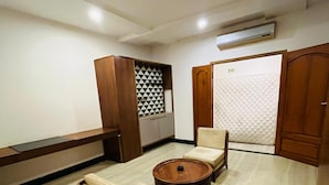 Una habitación con un armario de madera, un papel pintado decorativo, un sofá, una mesa redonda de centro y un ropero.