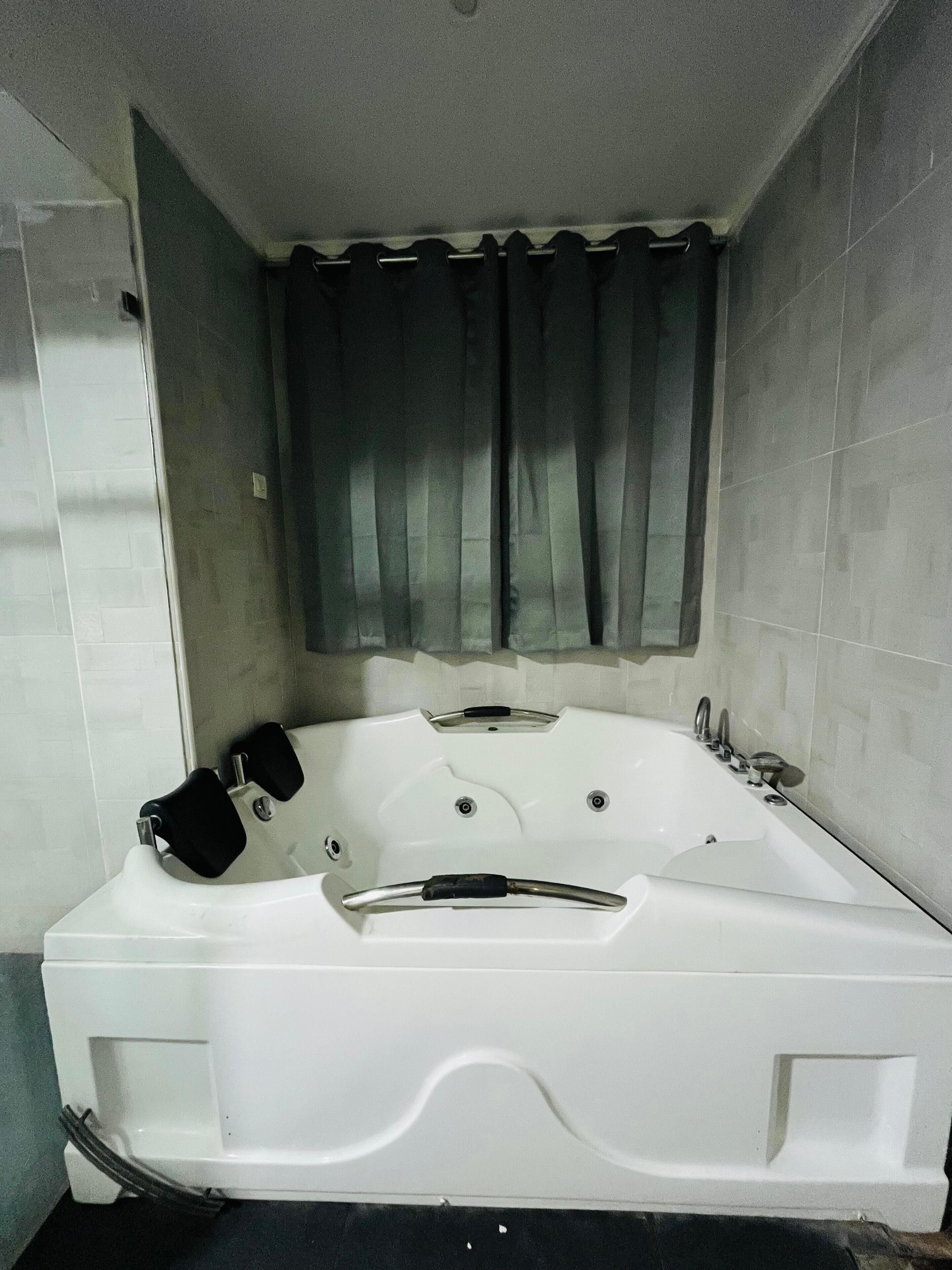 Bagno con una vasca da bagno bianca ampia, cabina doccia e finestra con tende.