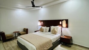 Un dormitorio con una cama grande, un ventilador de techo, una mesita de noche, una silla y una pequeña mesa.