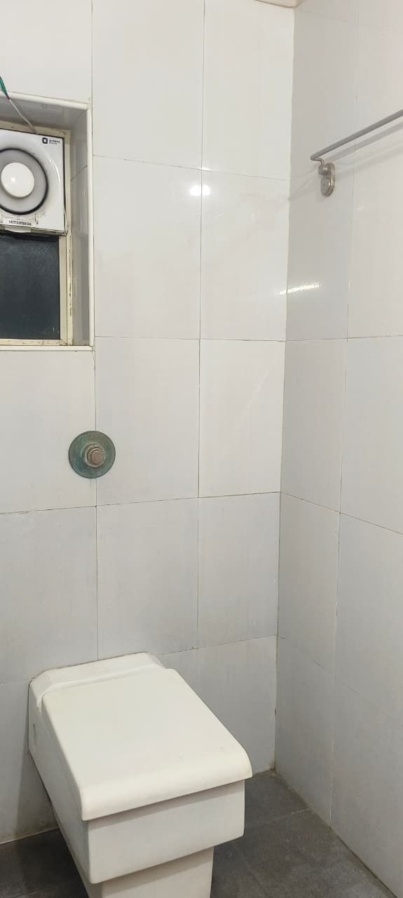 A small, white bathroom with a toilet, a shower area, and a ventilation unit on the wall.