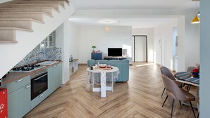 Eine moderne Küche mit Essbereich, einer Couch und einem Fernseher im Hintergrund.