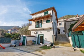 Un edificio de dos pisos con un balcón, una puerta y un pequeño espacio al aire libre con mesa y sillas.