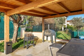 Un patio al aire libre con una pérgola de madera, una parrilla, un horno de pizza y una zona de estar.