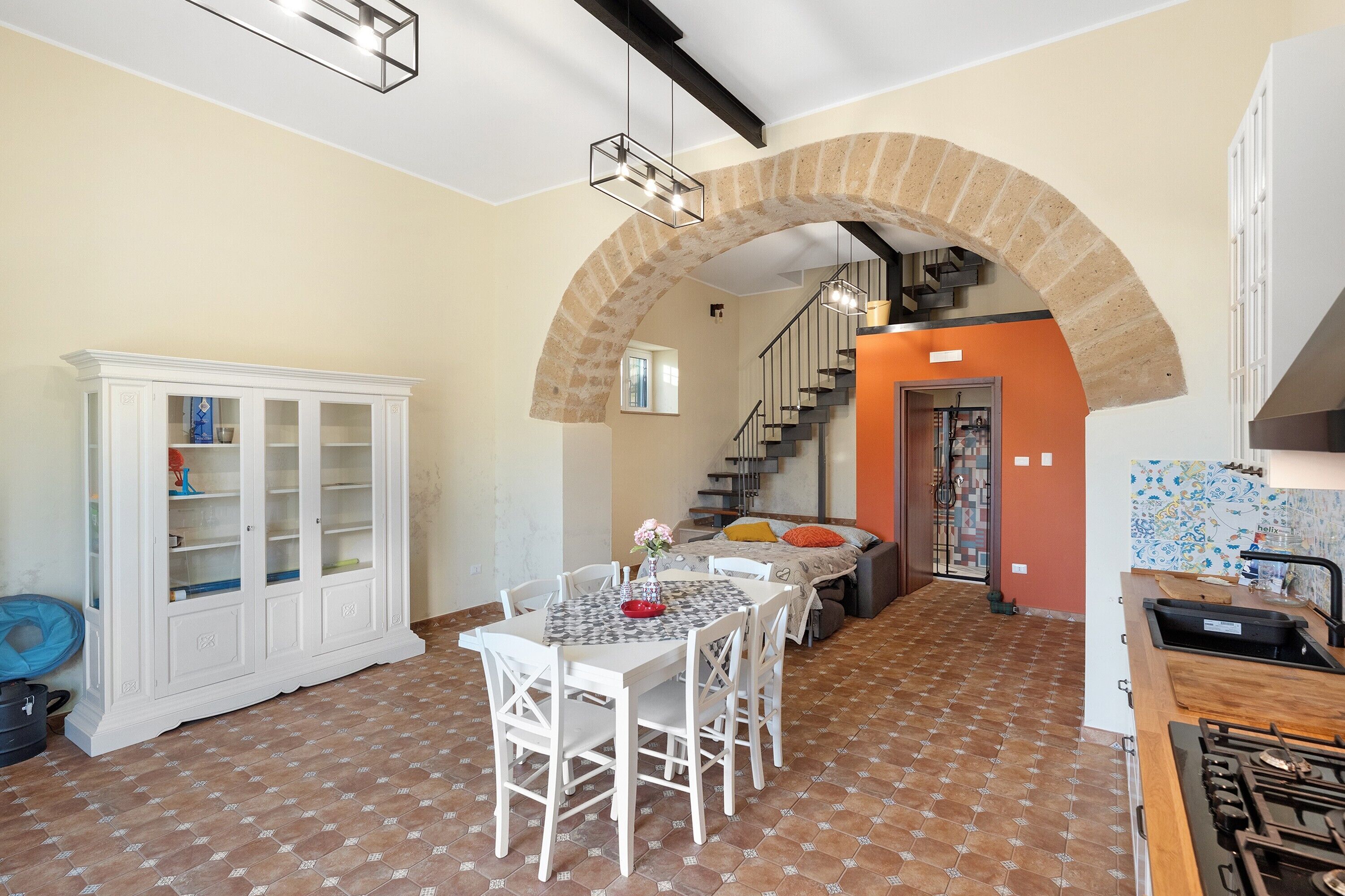 A dining area with a table and chairs, a white cabinet, a staircase, and a kitchen area with a stove.