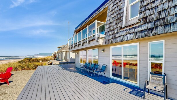 Ein Strandgrundstück mit einer Holzdielen-Terrasse, Sitzgelegenheiten im Freien und großen Fenstern mit Meerblick.