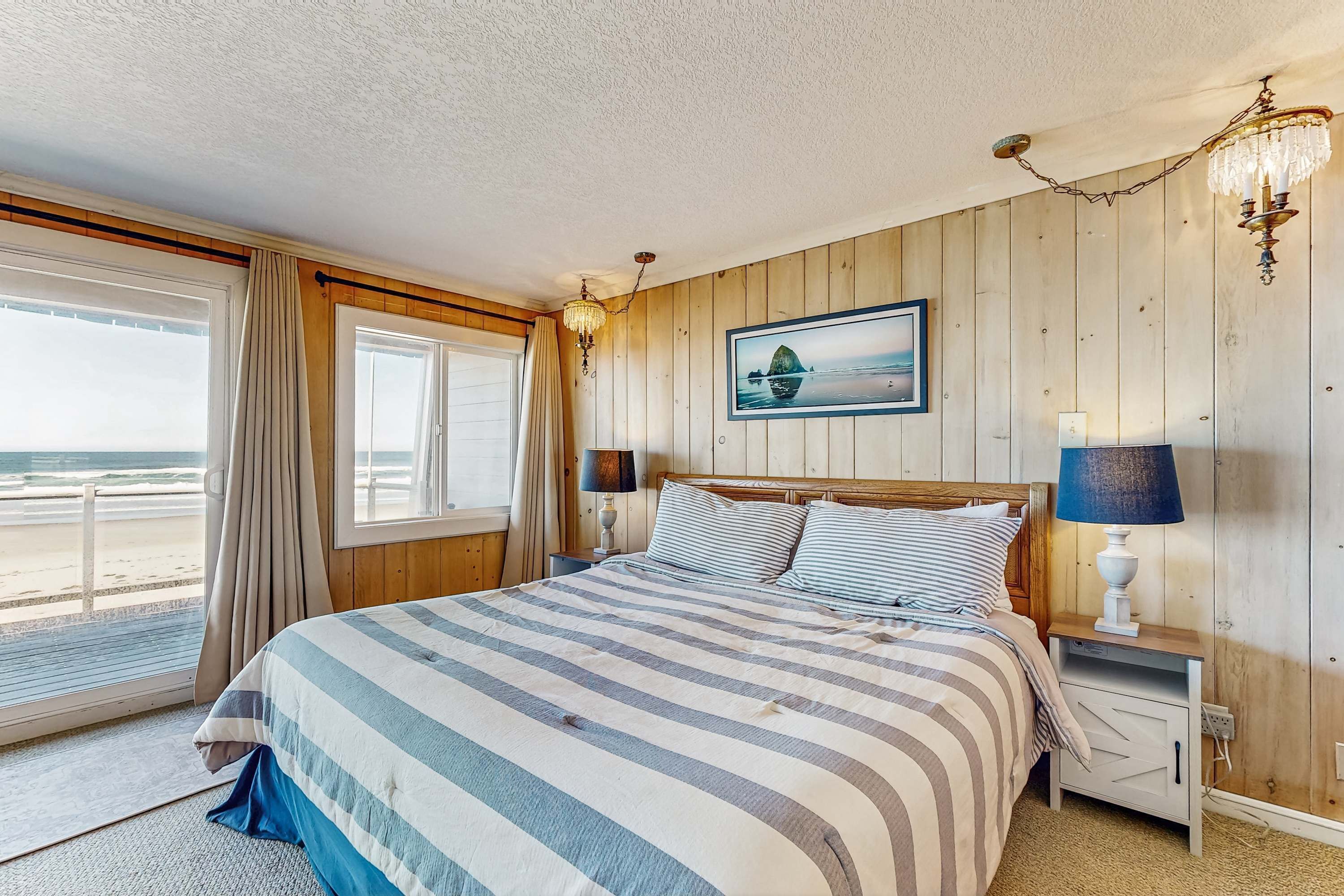Un dormitorio con una cama grande, paredes de paneles de madera, vista a la playa y un candelabro.