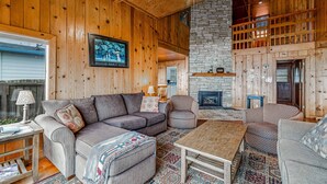 Interior acogedor de una cabaña con techo de madera, chimenea de piedra y zona de estar cómoda con sofá y sillones.