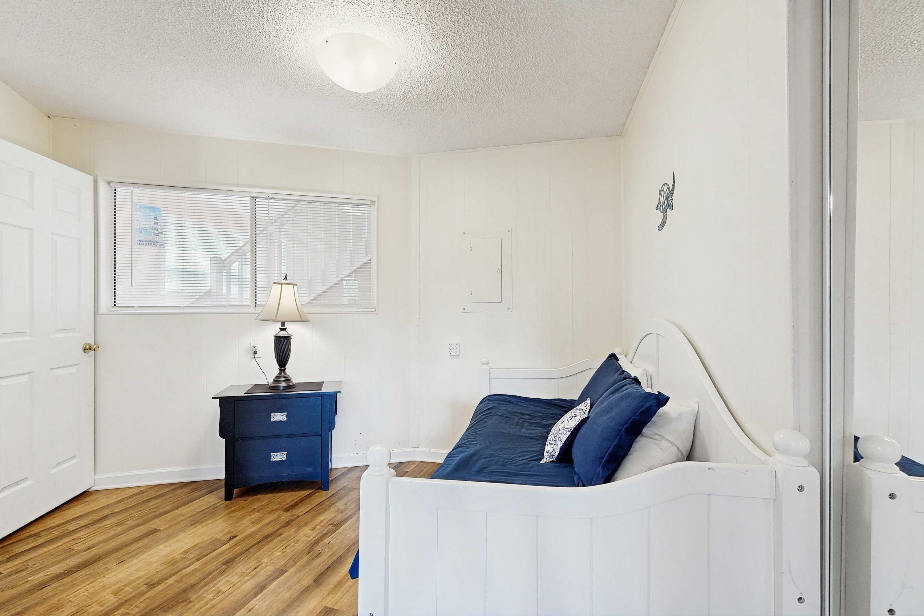 A bedroom with a white bed, a blue nightstand, and a window with blinds.