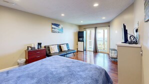 Ein Schlafzimmer mit Bett, Kommode, Schreibtisch, Stuhl, Mikrowelle und Blick ins Freie.