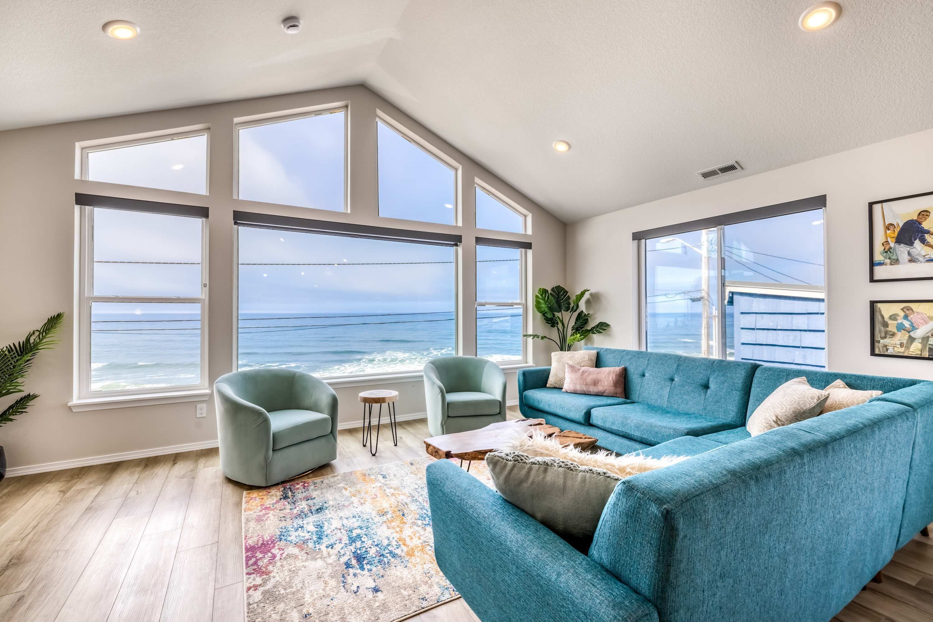 A spacious living room with large windows offering ocean views, a teal sofa, and a small coffee table.