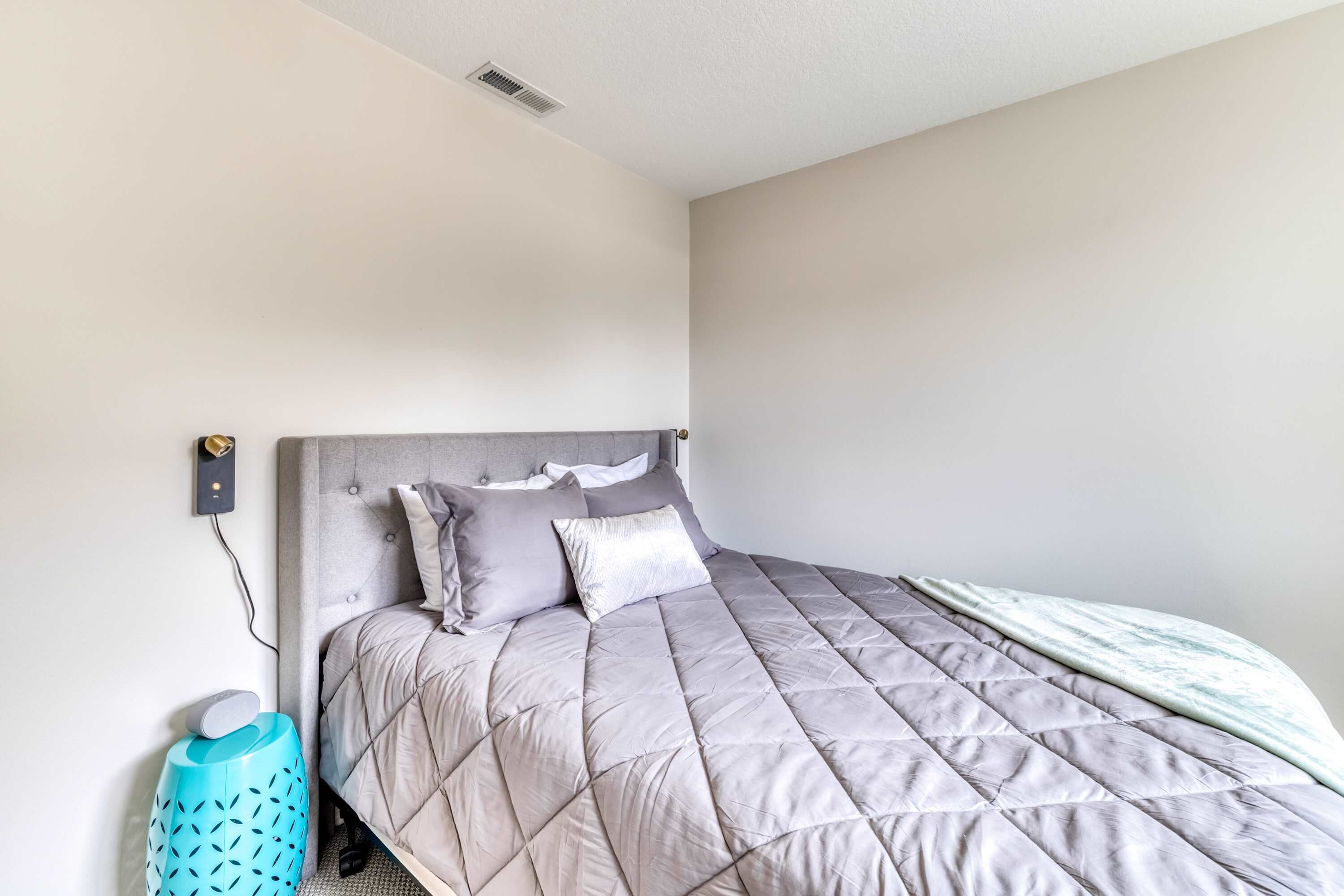 A bedroom with a bed, a headboard, a wall socket, and a trash bin.
