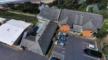 An aerial view of a coastal property with multiple buildings, a parking lot with several cars, and a beach in the background.
