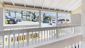 Un espace extérieur abrité, doté d’une rambarde blanche, un parking avec plusieurs voitures et des arbres en arrière-plan.