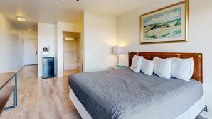 Une chambre d’hôtel avec un grand lit, un tableau au mur, un bureau avec une lampe et un petit réfrigérateur.