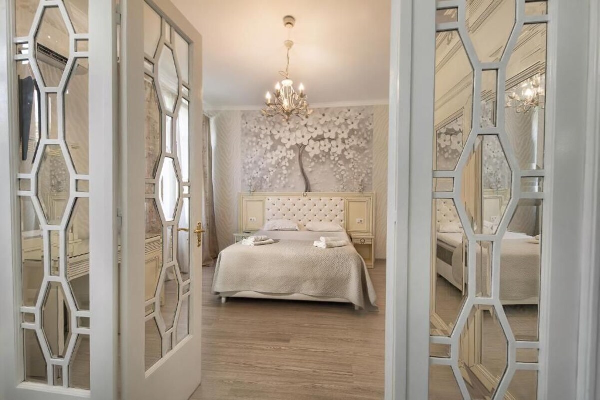 A bedroom with a large bed, a chandelier, and a decorative wall.