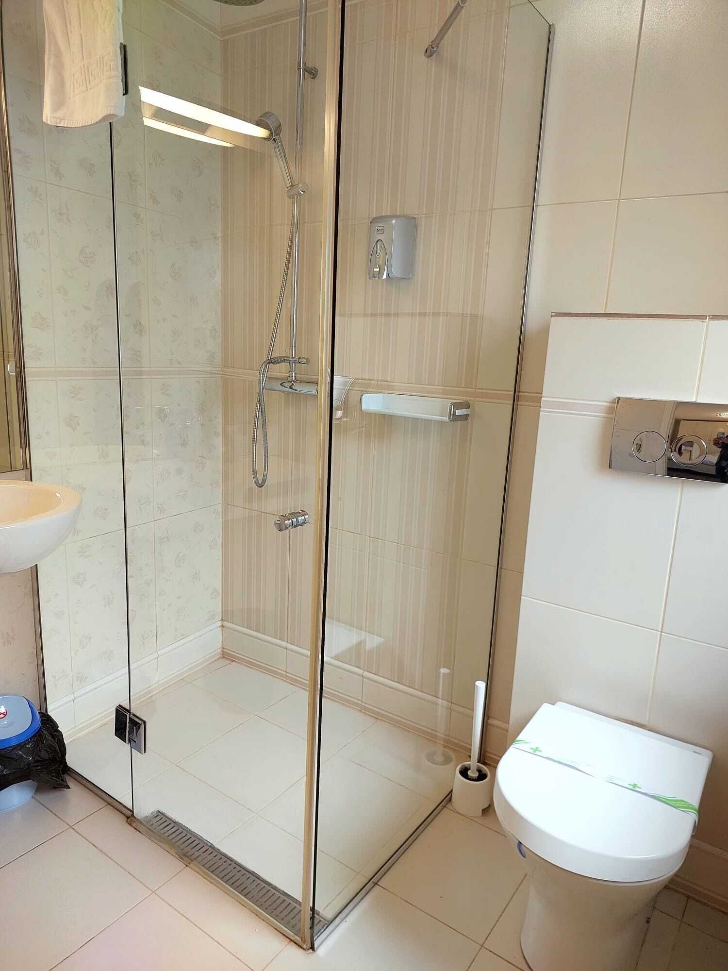 A bathroom with a glass-enclosed shower, a white toilet, and a sink with a towel hanging above it.