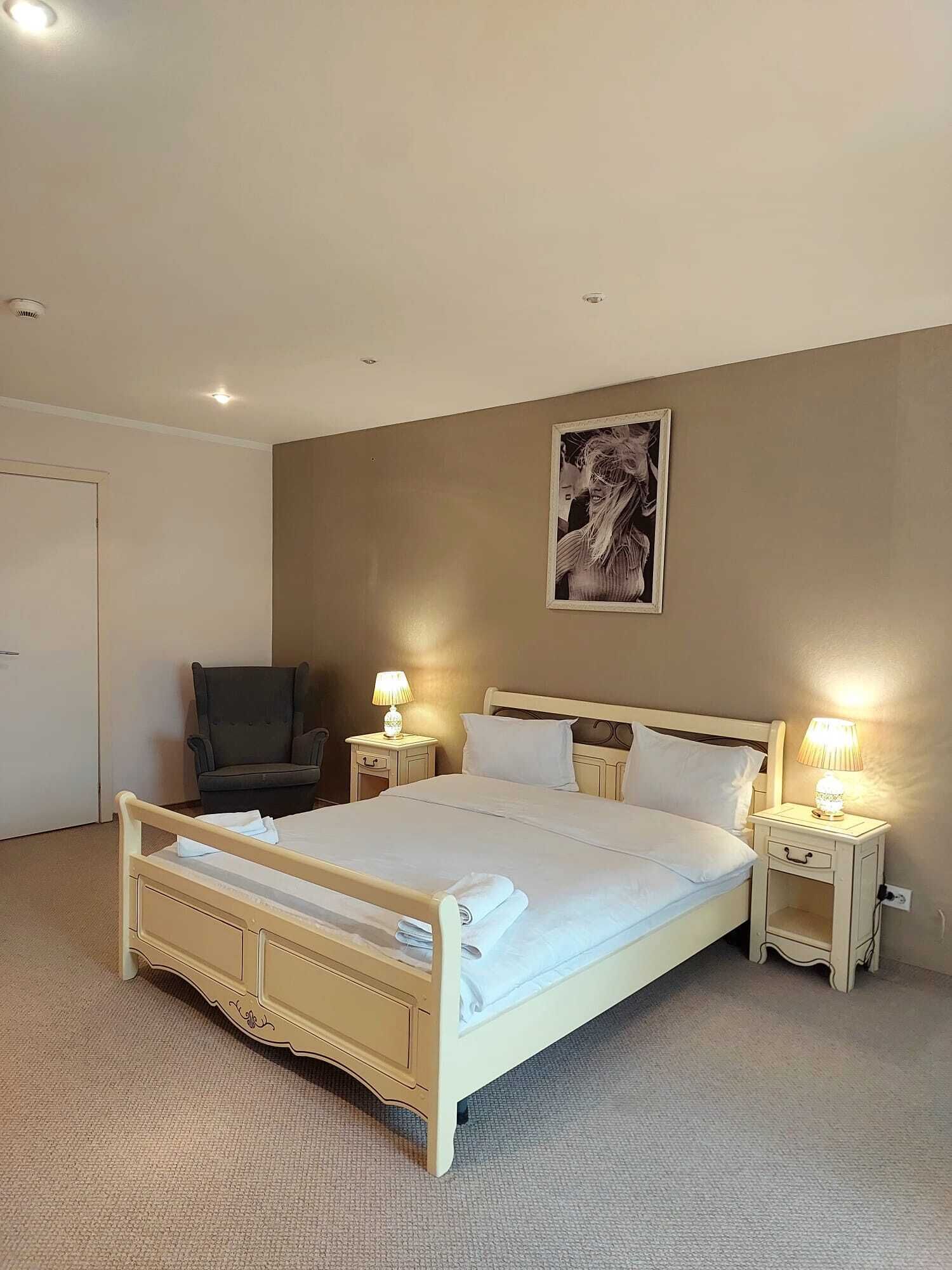 A hotel room with a large bed, two bedside tables with lamps, a chair, and a wall-mounted artwork.