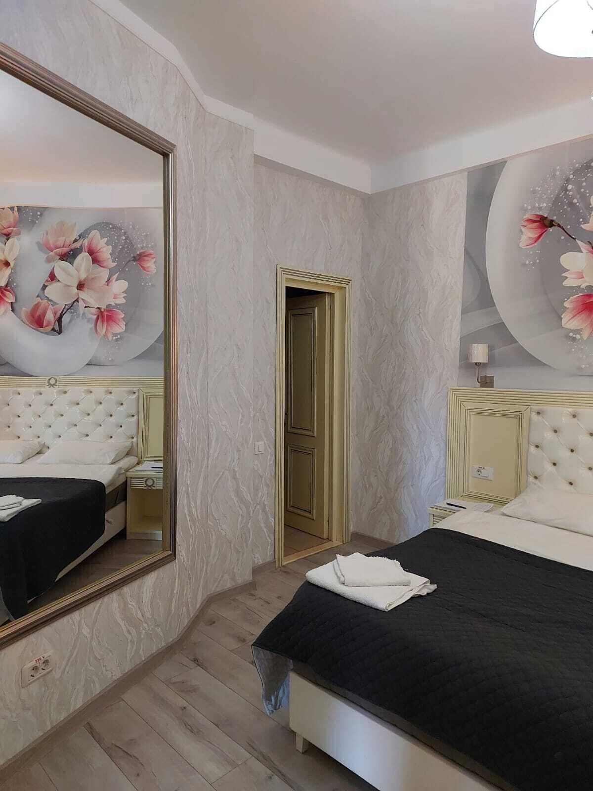 A hotel room with a large mirror, a bed with a black bedspread, a nightstand, and a wall with floral artwork.