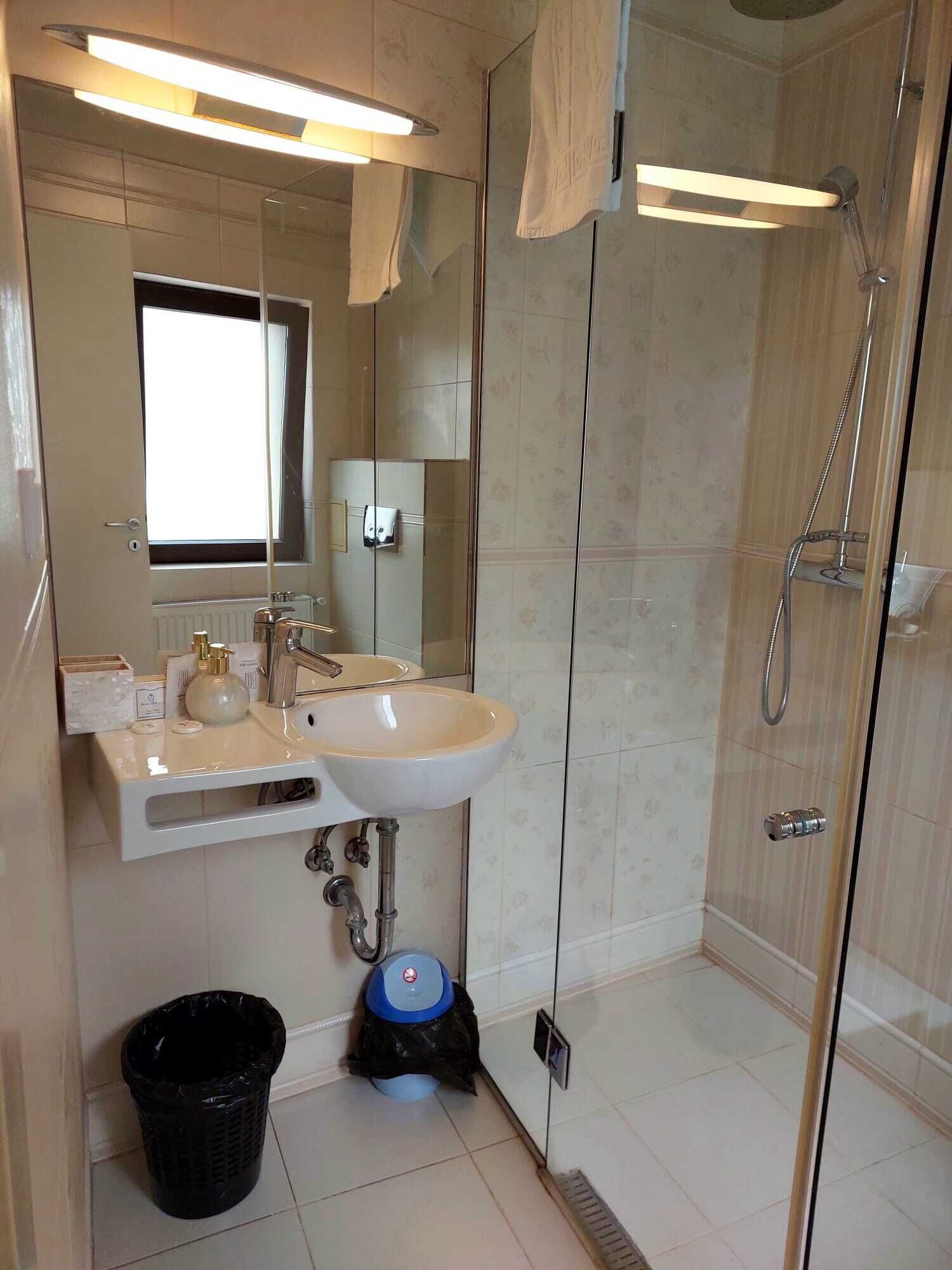 Een moderne badkamer met een douchecabine van glas, een wastafel met spiegel en een prullenbak.