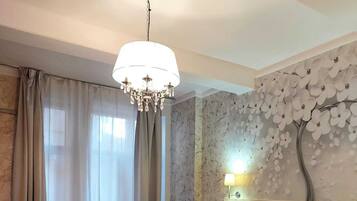 Una habitación de hotel con una cama grande, dos mesitas de noche, una araña y una pared decorada con un mural floral, además de una ventana con cortinas.