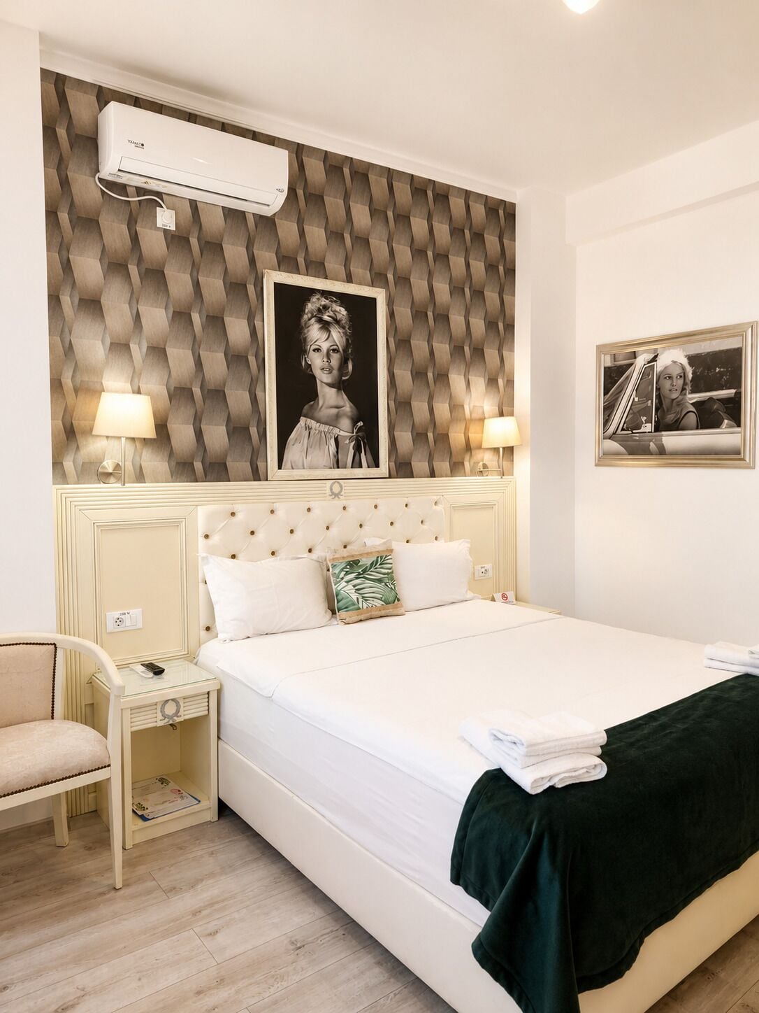 Una habitación de hotel con cama, mesitas de noche, lámpara, aire acondicionado instalado en la pared y un cuadro enmarcado.