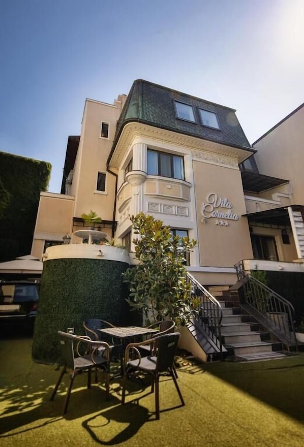 A hotel named "Vila Cornelia" with a modern architectural style, featuring a prominent entrance, a staircase, and outdoor seating area. - Carol Boutique (Bucharest)