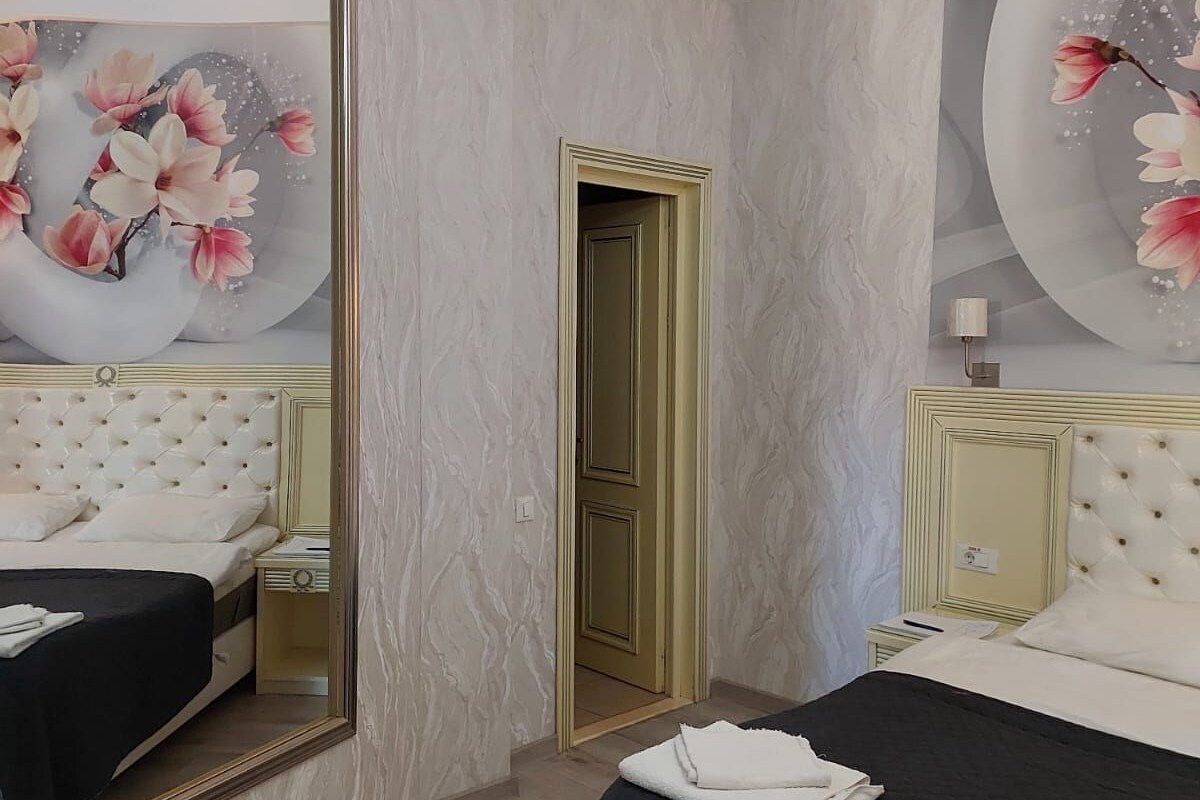 A hotel room with a large mirror, a bed with a black bedspread, a nightstand, and a wall with floral artwork.