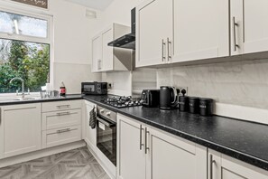 Cocina moderna con armarios blancos, encimera negra y ventana con vistas a la vegetación.
