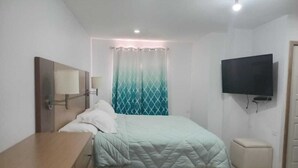 Un dormitorio con cama, mesita de noche, televisor en la pared y cortina.